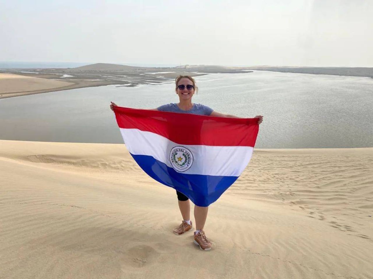 La periodista de GEN/NaciónMedia con la bandera paraguaya en las dunas junto a un oasis en el desierto. @marletorres29